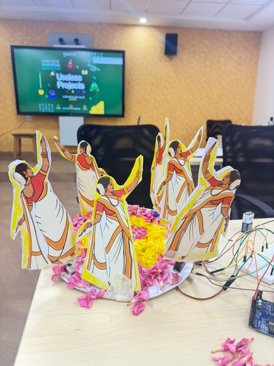 The finished Servo Naatyam project — six Thiruvathira figures arranged around a pookalam with Arduino and wires visible